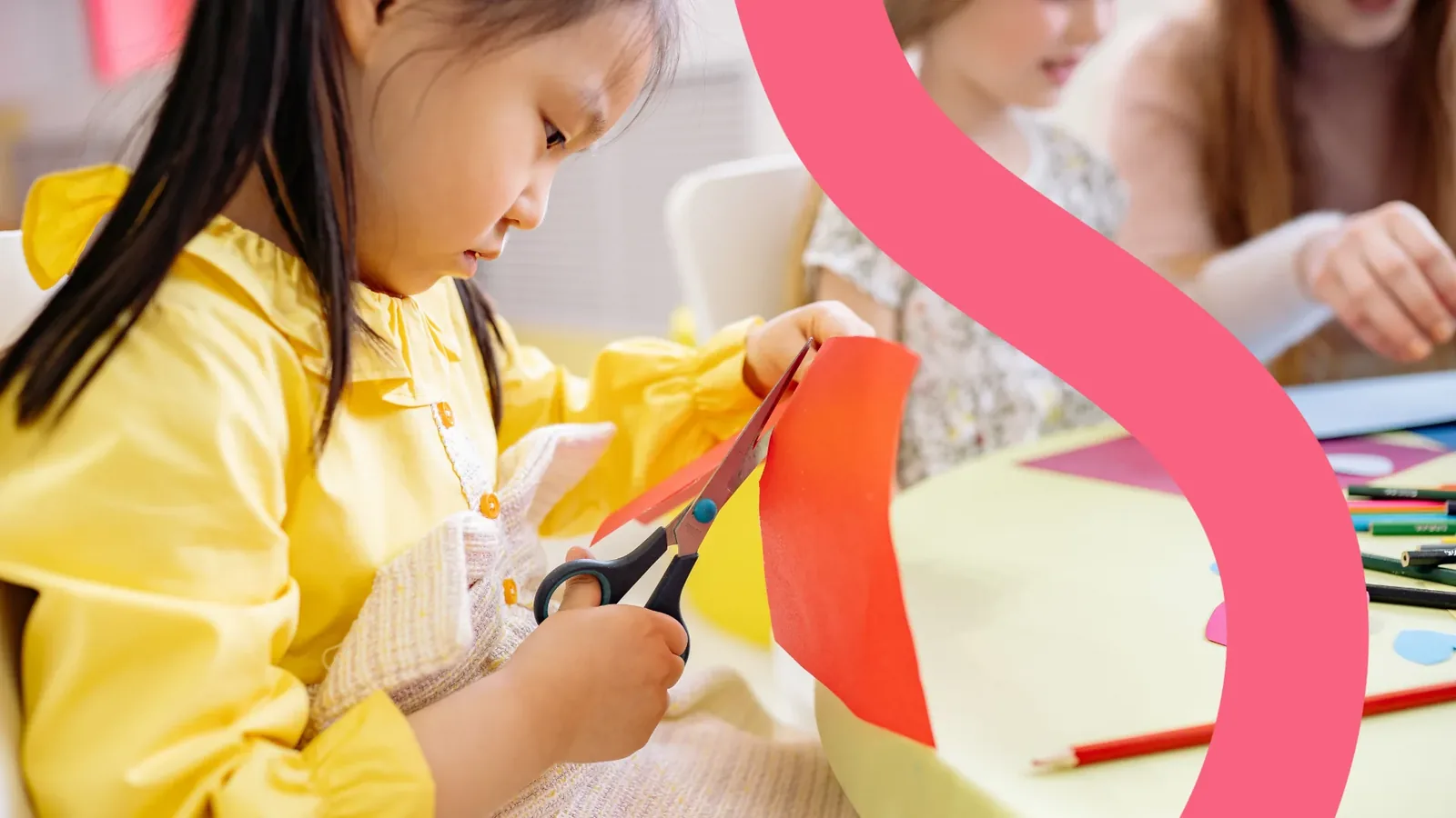 Niña con camisa amarilla recortando papel rojo con unas tijeras